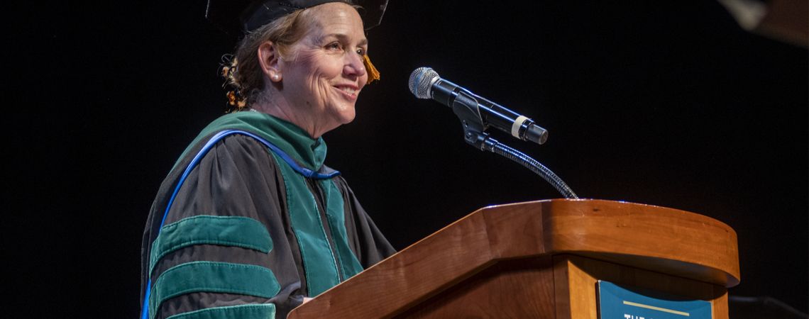 Dean Barbara Bass at podium wearing her regalia